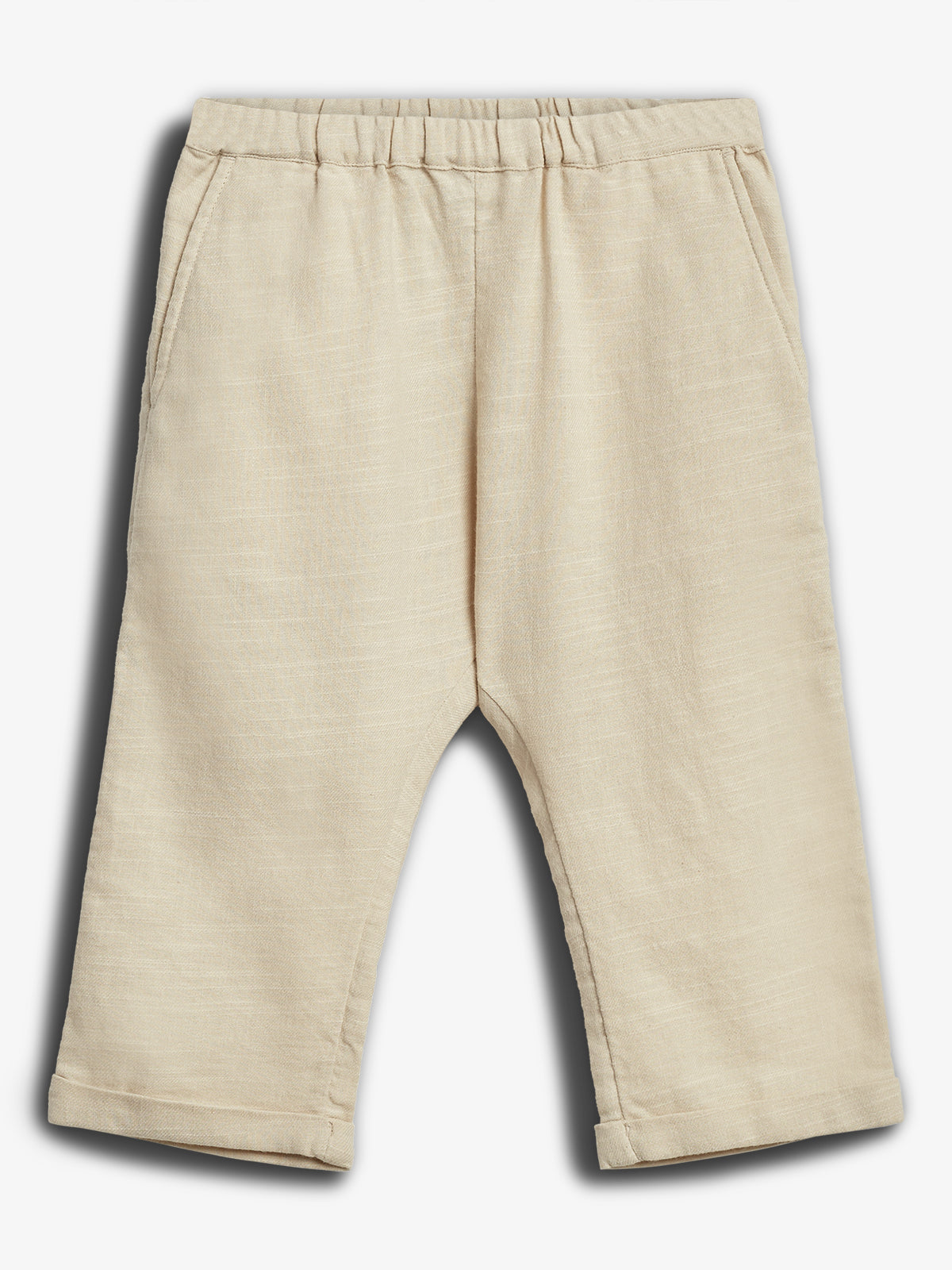 Beige, løstsiddende bukser ligger fladt med elastisk linning og sidelommer; stoffet ser let og komfortabelt ud, placeret mod en neutral baggrund.
