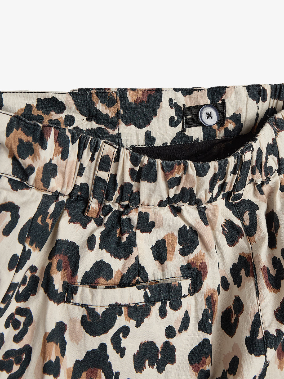 Leopard-print shorts feature an elastic waistband with a button detail above a pocket. The fabric pattern consists of black and brown spots on a beige background, against a plain white setting.