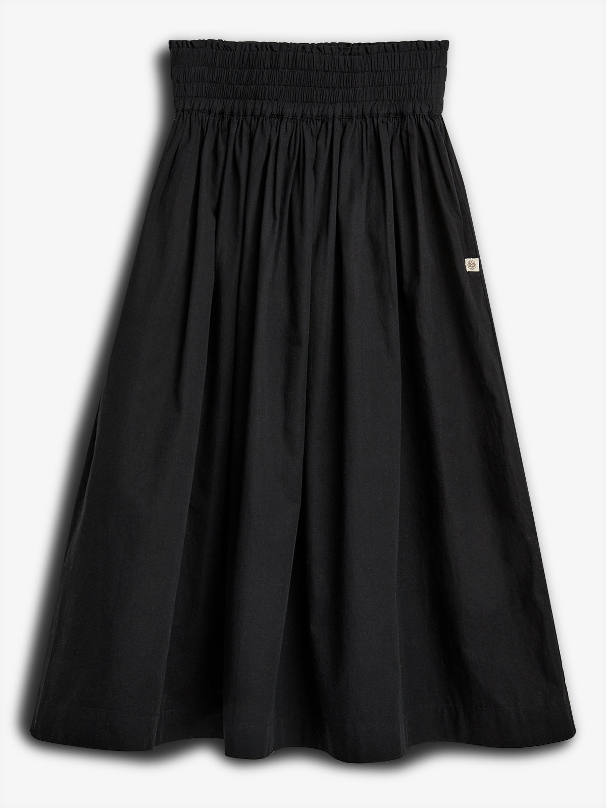 A black skirt hangs against a white background. It has a ruched waistband, a full, gathered silhouette, and a small square logo patch on the side.