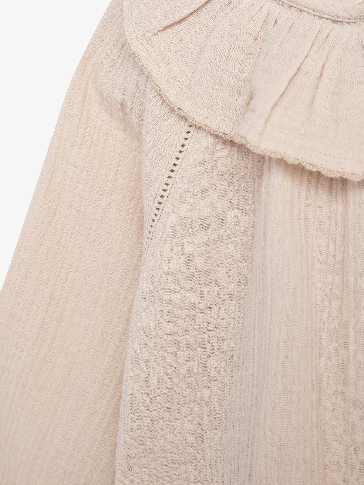 A beige, textured fabric with a ruffled edge, likely a garment detail, displays fine stitching and lace trim in a soft, neutral-toned close-up view.