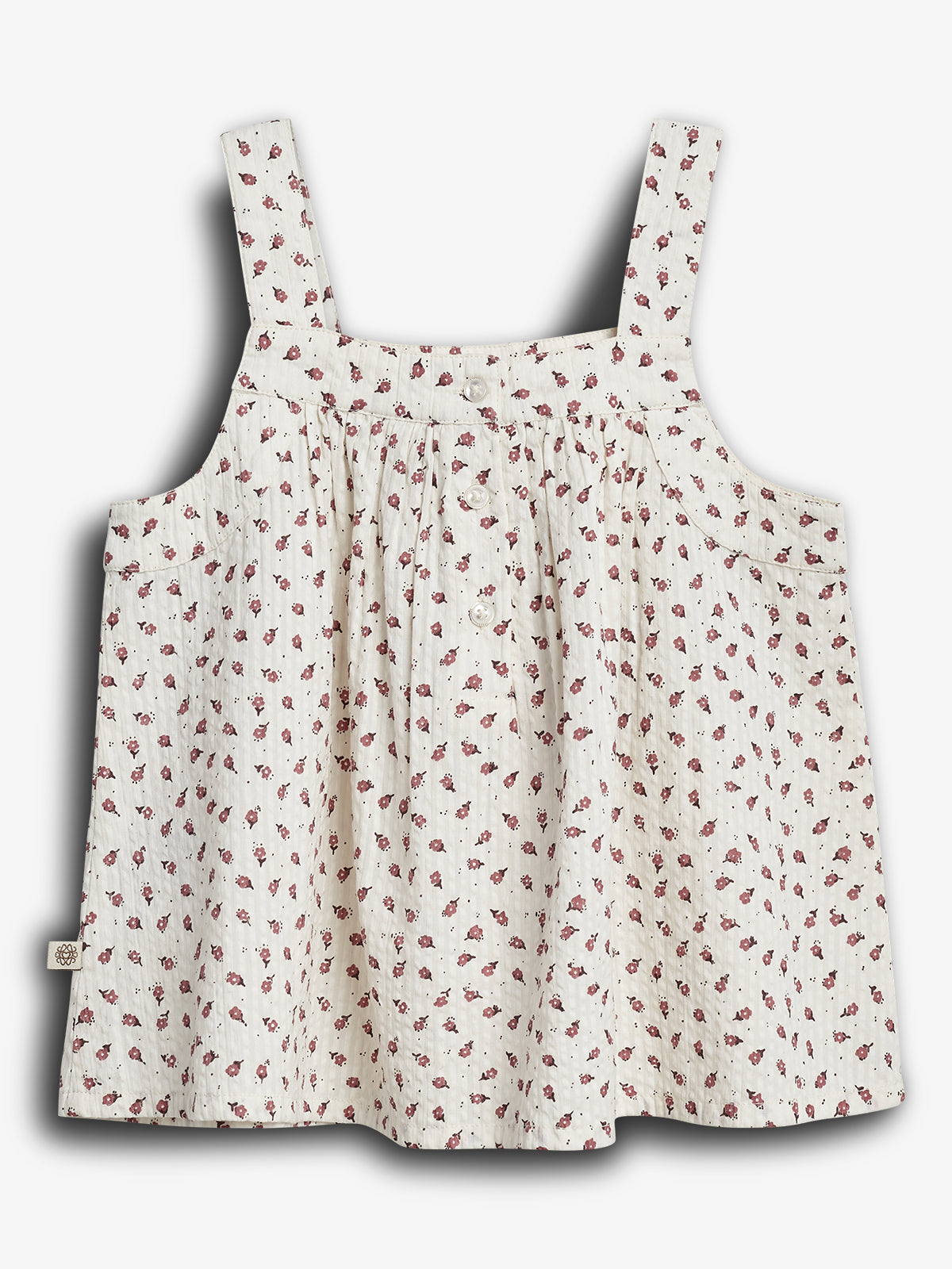 A sleeveless, white, floral-patterned blouse with shoulder straps is displayed on a plain white background. The blouse features small red flowers and a gathered, flowing design.