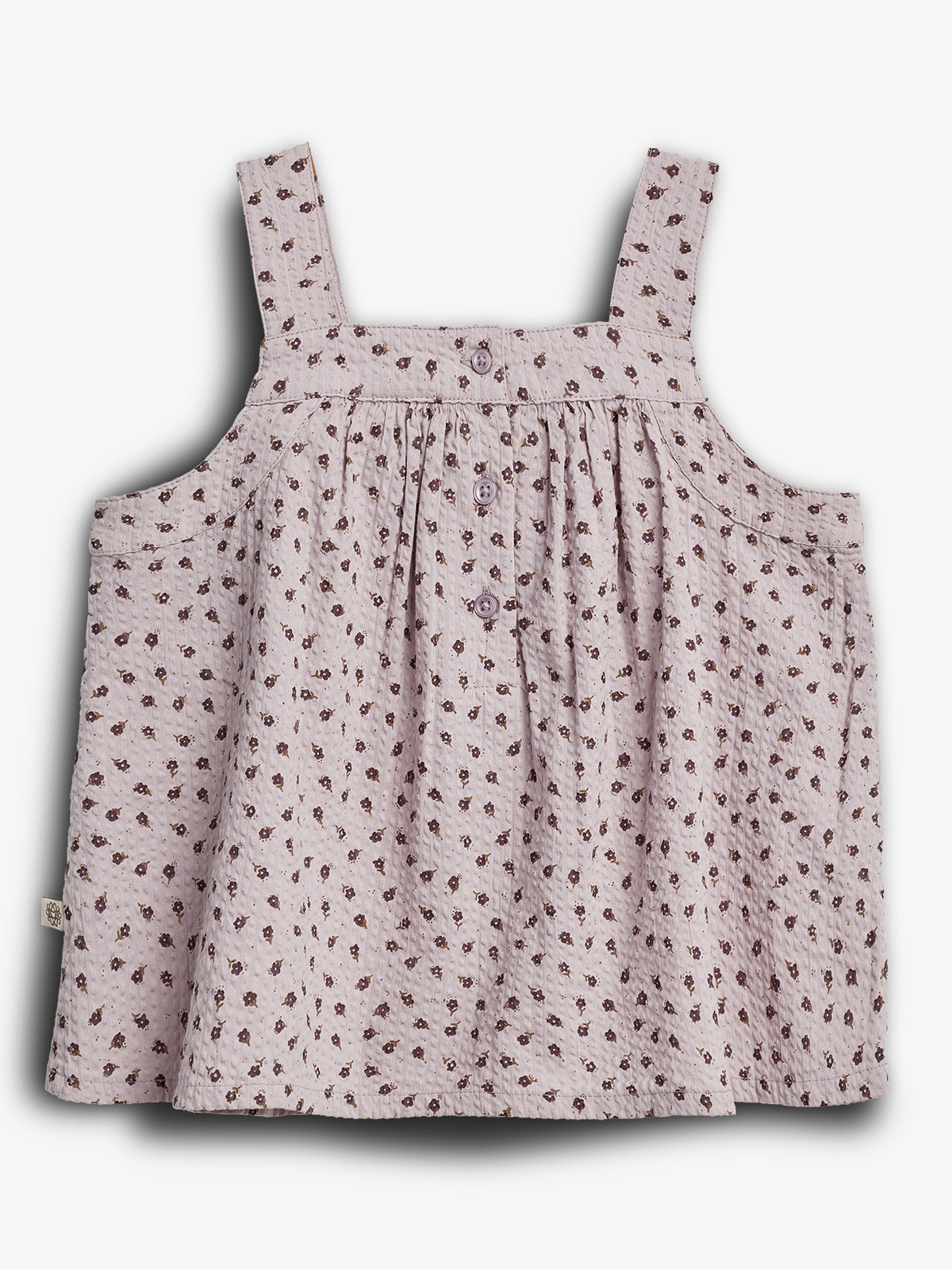 Lyslilla top med små blomsterprint og brede stropper. Tre knapper foran pynter designet. Toppen hænger løst og skaber en let og luftig stil i et neutralt, hvidt miljø.