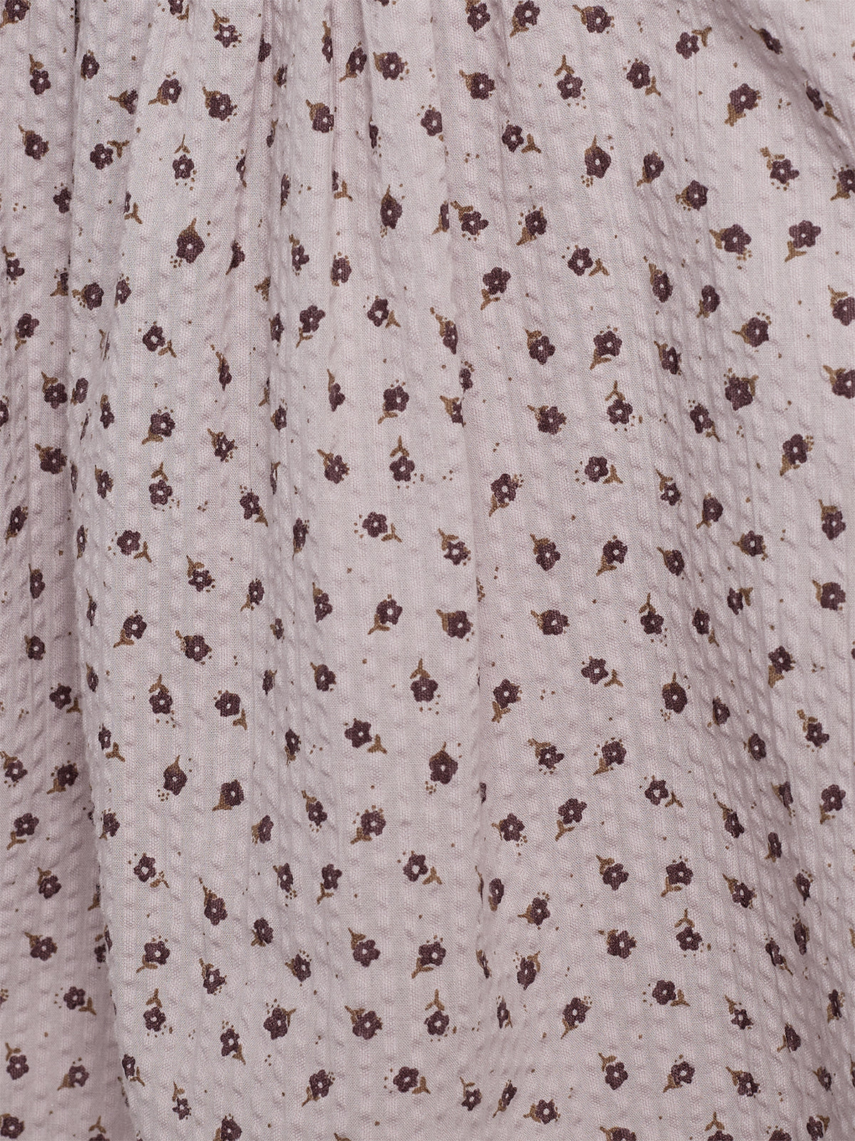 A textured fabric with a pattern of small, dark flowers evenly distributed across a light background. The material is gathered, likely part of a garment, creating soft folds.