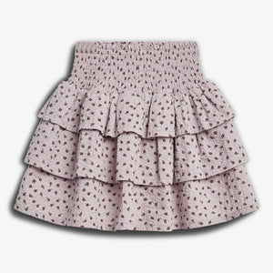 A tiered, floral-patterned skirt with a shirred, elastic waistband, displaying a soft-textured fabric. It rests against a plain white background, highlighting its light pink color and brown floral details.