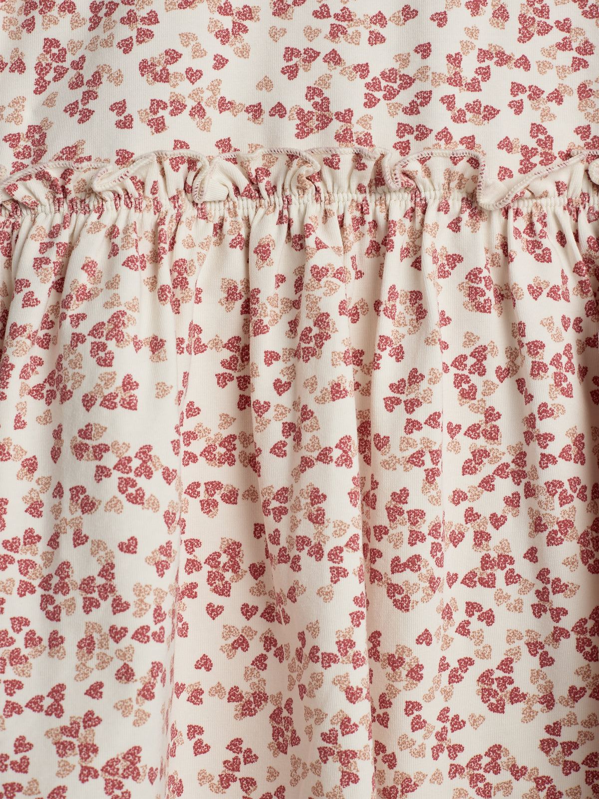 Et stofmønster viser røde og beige blomster på hvid baggrund. Stof er samlet i en rynke, hvilket giver struktur og bevægelse i et ubrudt mønster i et harmonisk design.