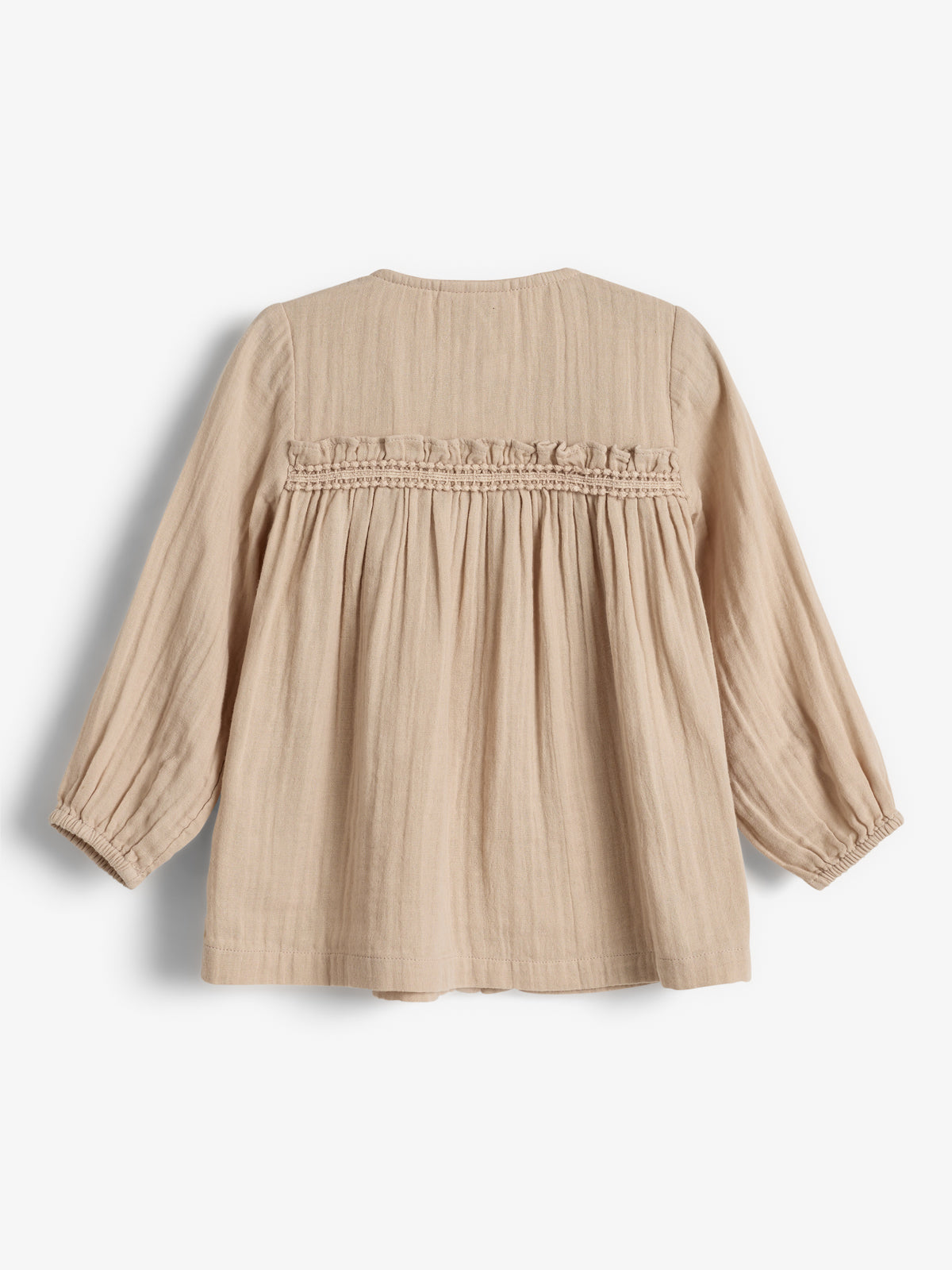 Beige skjorte med lange ærmer hænger ubevægelig mod en hvid baggrund. Den har rynker og en dekorativ kant på ryggen.