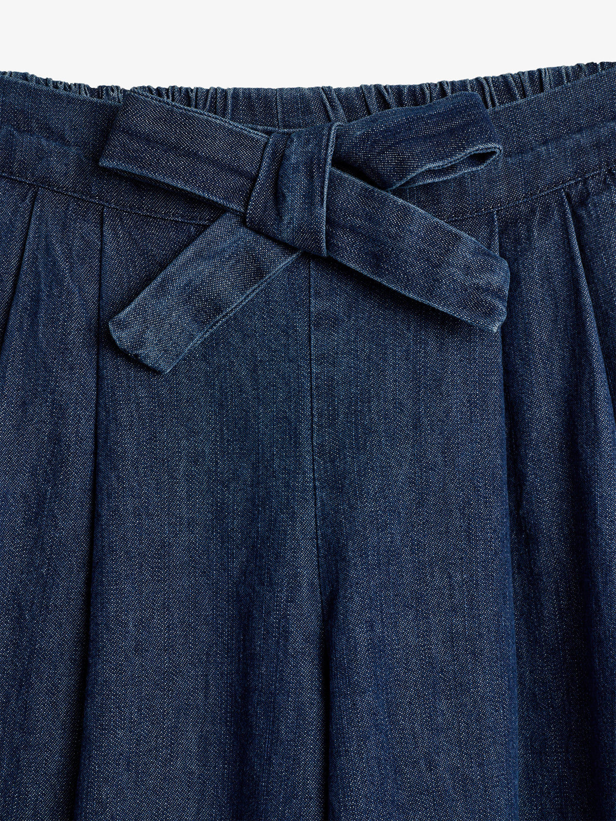 Et par mørkeblå denim bukser med en knytning i livet. Bukserne har plisserede detaljer og elastik i taljen. Baggrunden er ensfarvet lys.