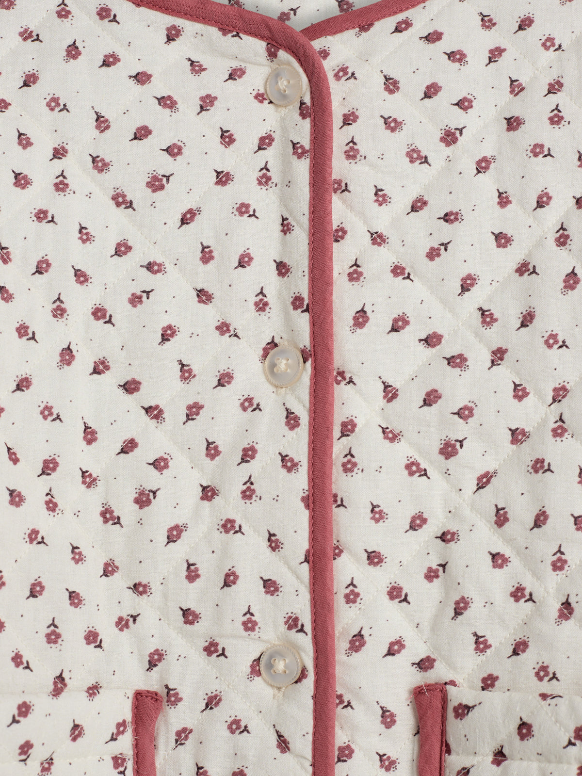 En quiltet jakke, dekoreret med små, røde blomstermotiver, er knappet fortil. Jakken er indrammet af mørkerøde kanter og knapper.