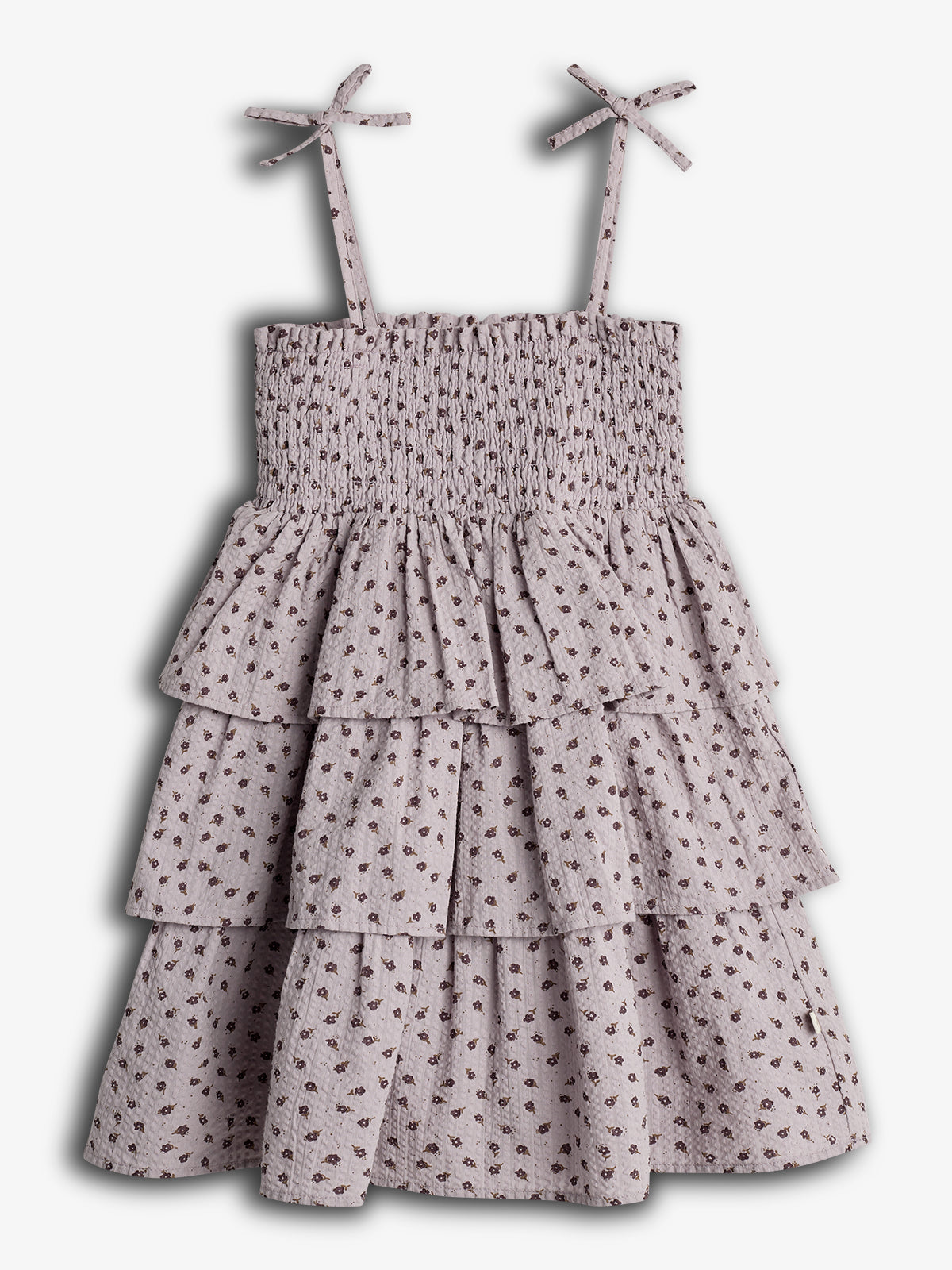Kjole med stropper og små sløjfer, blomsterprintede mønstre og flere lag flæser, hænger mod en neutral baggrund.