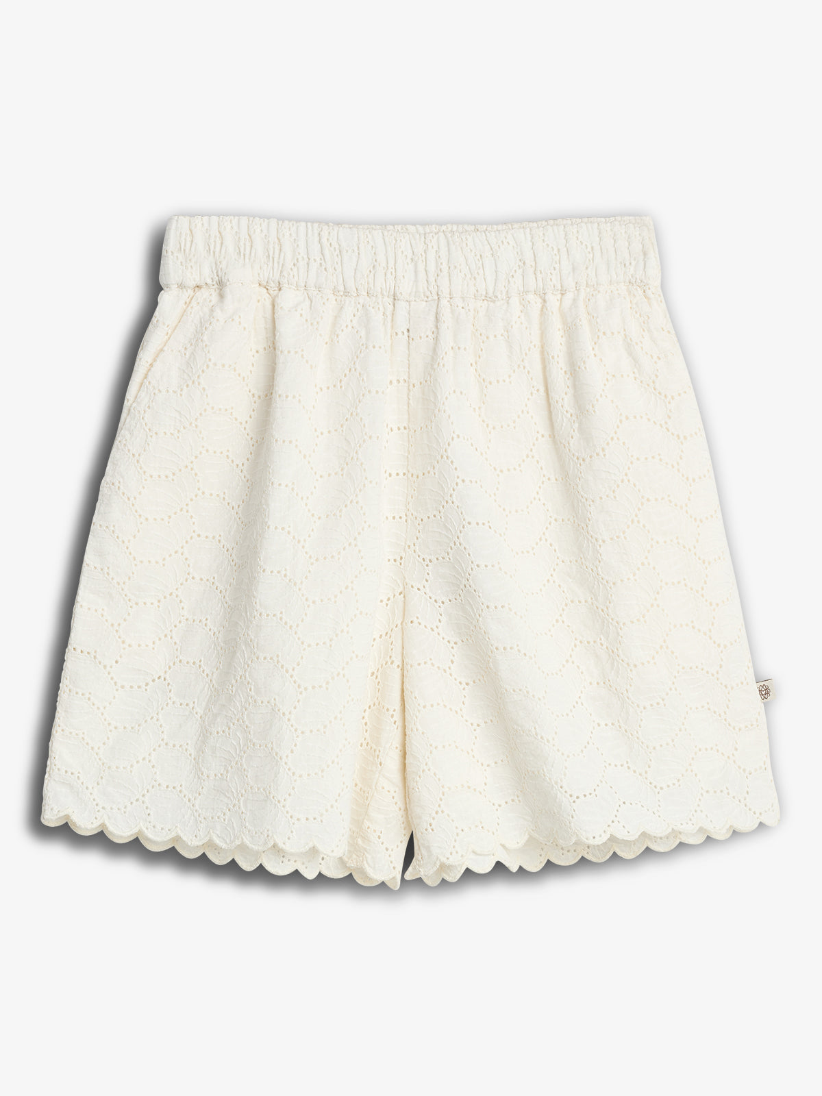 Hvide shorts med elastisk talje har et blødt blondemønster og bølgede kanter. De ligger fladt mod en grå baggrund.