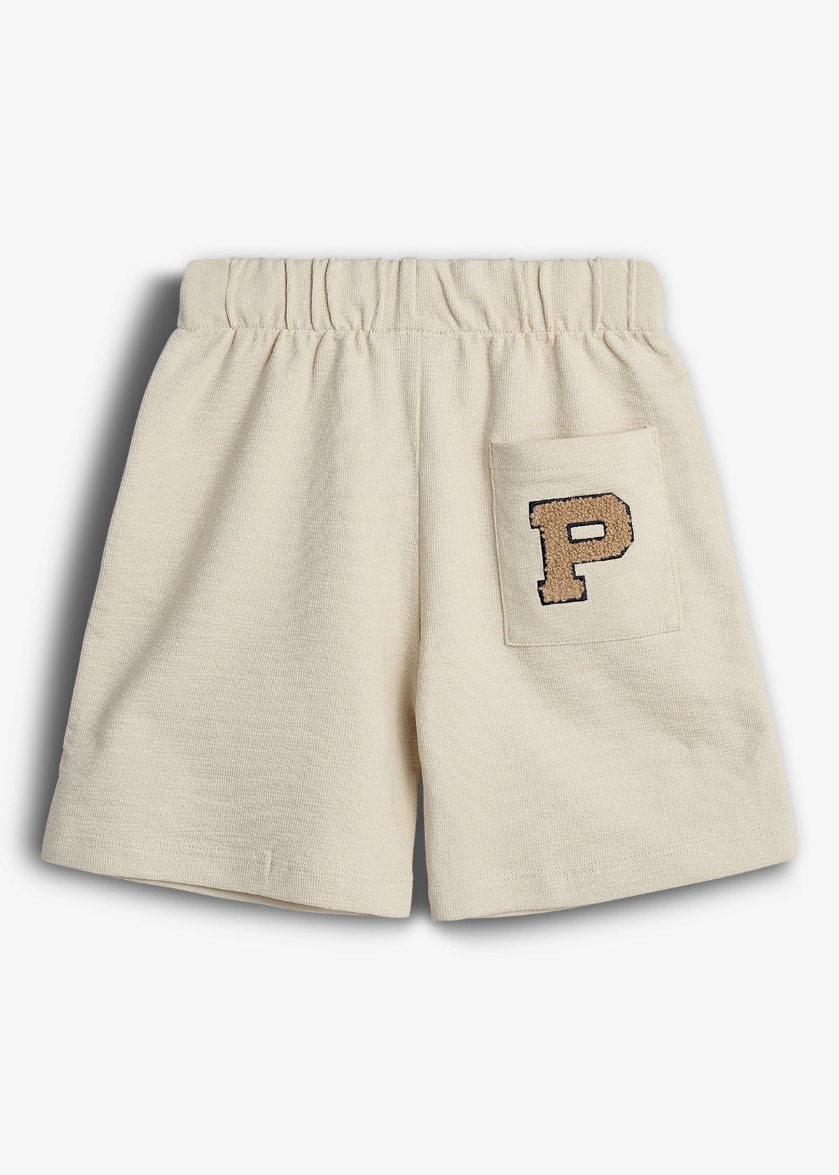 Beige shorts display an uppercase "P" emblem on a pocket. Surrounded by a plain background, these shorts feature an elastic waistband suitable for casual wear.