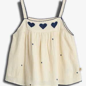 A cream-colored sleeveless top adorned with navy blue hearts and scalloped edges hangs against a plain backdrop.