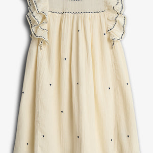 A cream-colored dress with ruffled sleeves is adorned with small, dark heart patterns and stylish embroidery. It hangs against a plain white background, displaying its elegant design and craftsmanship.