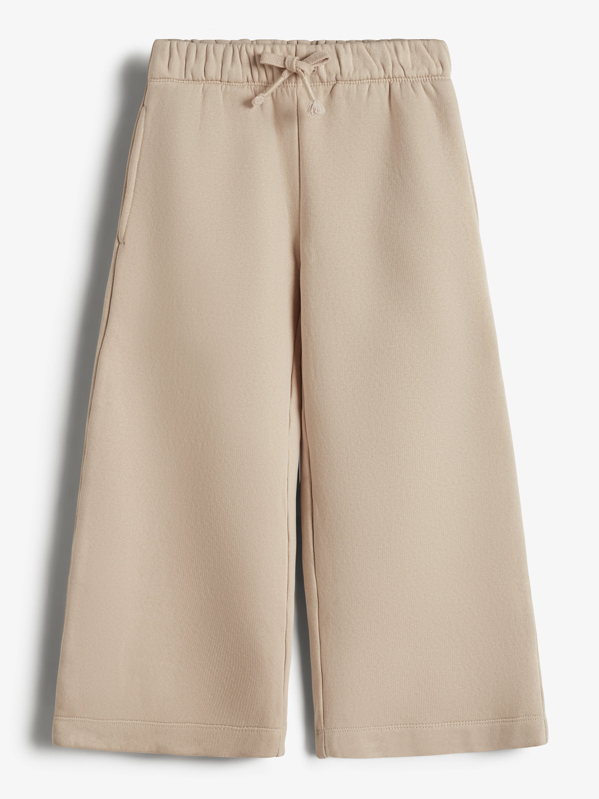 Beige culotte-bukser hænger stille; de har elastisk talje med snøre og sidelommer. Placeret mod en enkel, hvid baggrund.