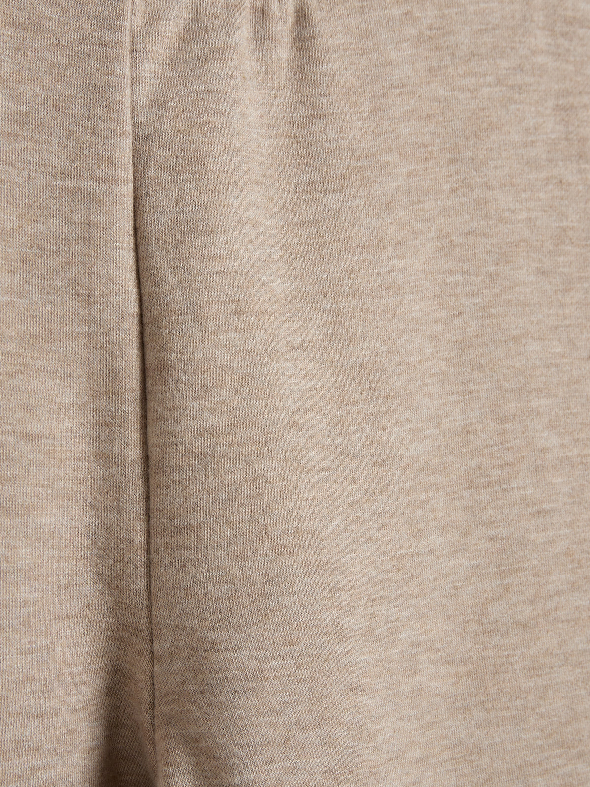 Beige stof med lodret fold, der skaber en blød tekstur. Materialet er jævnt og ensartet, hvilket indikerer afslappet beklædningsdesign i et neutralt miljø.