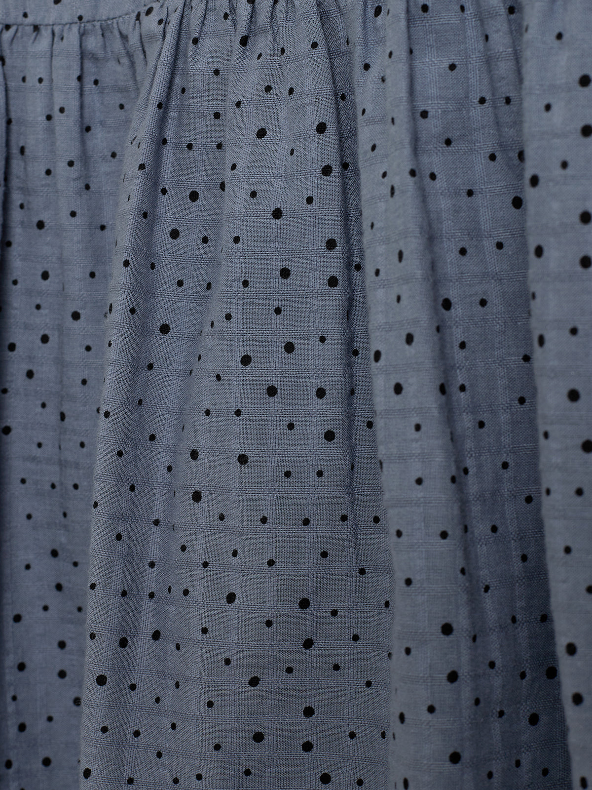 Blue fabric with black polka dots drapes softly, showing a grid-like texture, creating subtle shadows and folds across its surface.