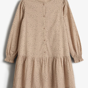 En beige kjole med sorte prikker hænger stille. Knappet foran med lange ærmer og rynket nederdel. Baggrunden er neutral og lys. Tekst: "Minimango."