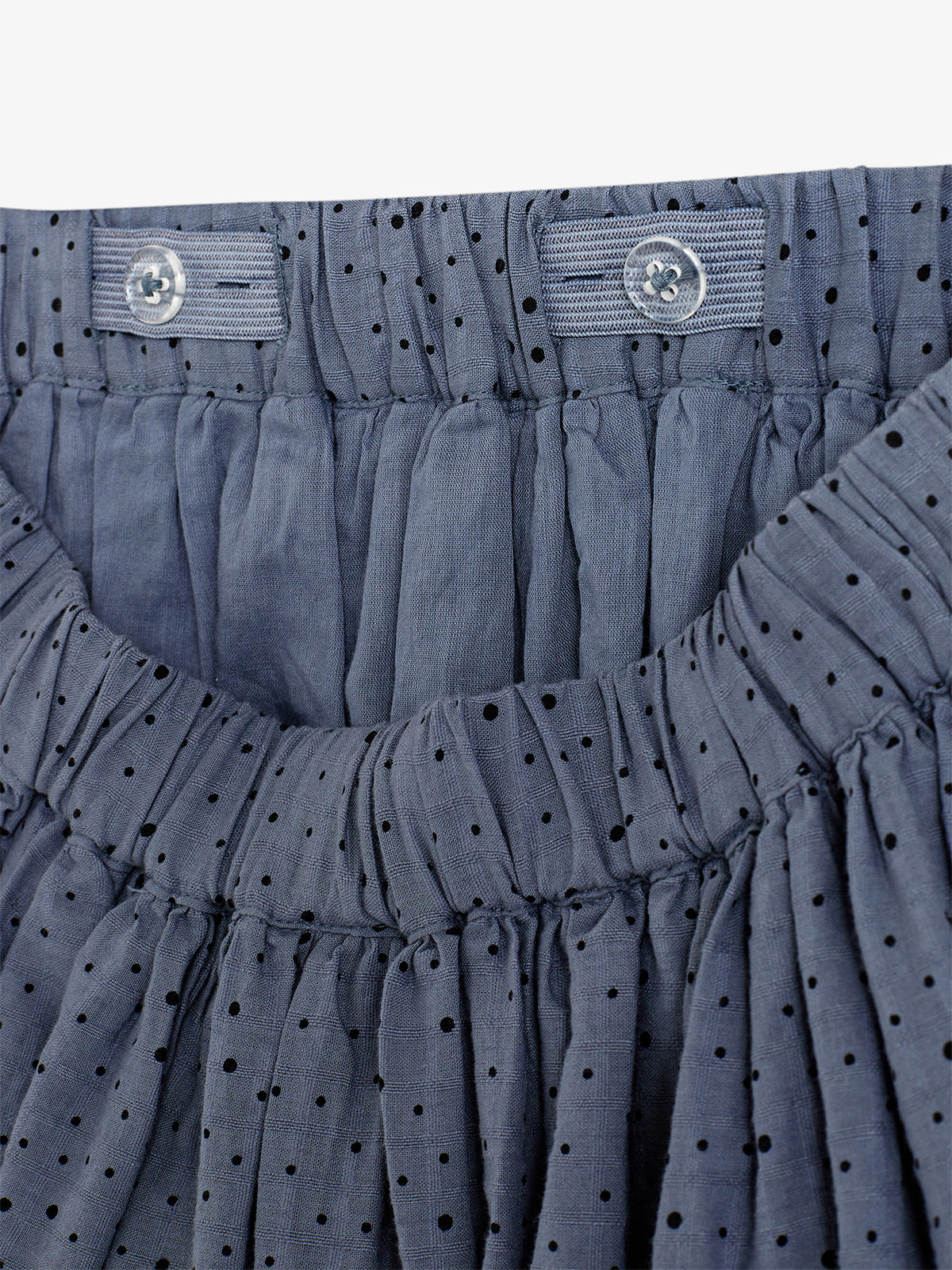 A blue fabric skirt is gathered at the waistband with two buttons securing it. The material features a pattern of small black polka dots, creating a textured appearance.