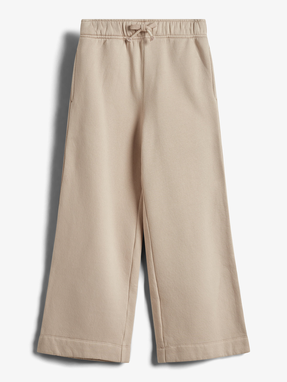 Beige bukser hænger mod en hvid baggrund. De har elastisk talje med snøre og to sidelommer. Bukserne har et afslappet og bredt snit, der når til ankellængde.