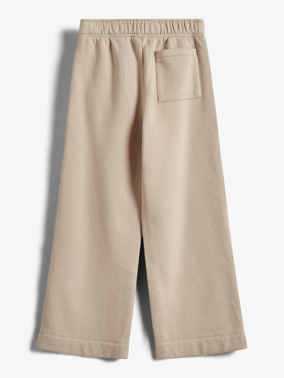 Bukserne hænger stille mod en lys baggrund. De er beige med en løs pasform, elastisk talje og en enkelt lomme på bagsiden øverst til højre.