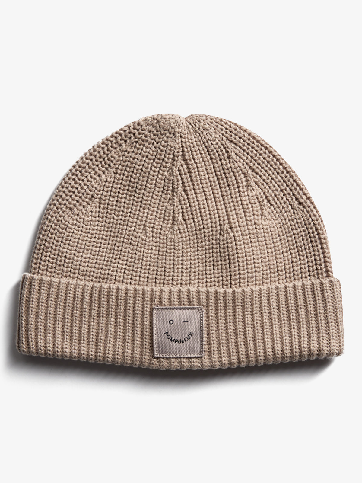 En beige strikket hue med et ombukket kant. På forsiden er der en mærkat med teksten "pOMPdeLUX" og en simpel ansigtsskitse. Baggrunden er helt hvid.