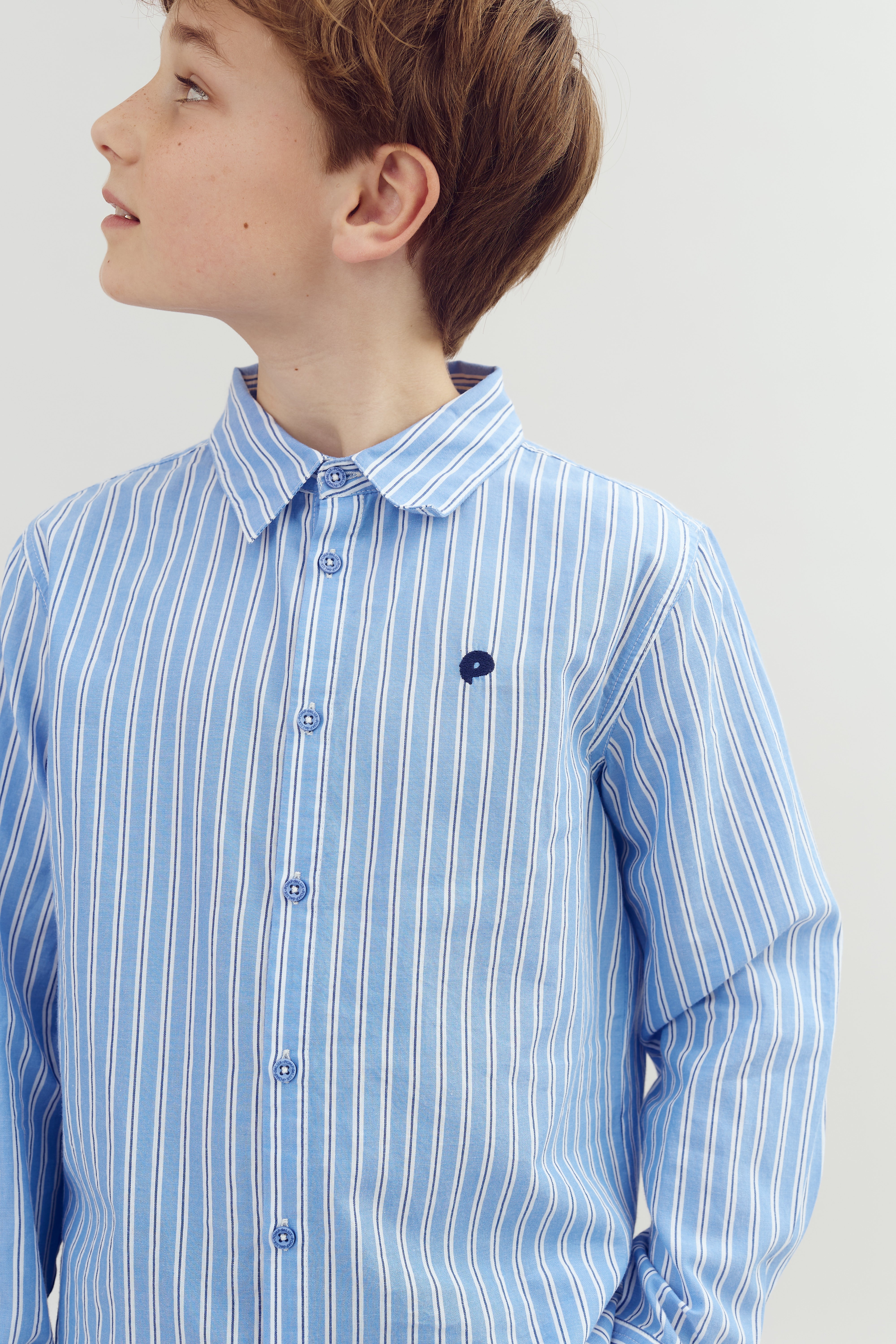 A child wearing a blue and white striped shirt looks to their left, set against a plain white background.